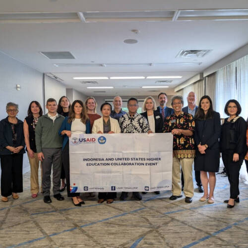 A group of people stands together in a conference room holding a banner that reads "Indonesia and United States Higher Education Collaboration Event," with USAID and other partner logos, representing a formal gathering focused on international academic pa